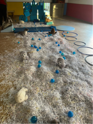 Instalación sensorial del Ártico en la Escuela Infantil Cancionero con papel triturado simulando nieve, peluches de focas y módulos de psicomotricidad azul.