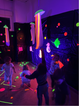 Niños explorando y jugando con medusas fluorescentes en la sala de luz negra de la Escuela Infantil Cancionero.